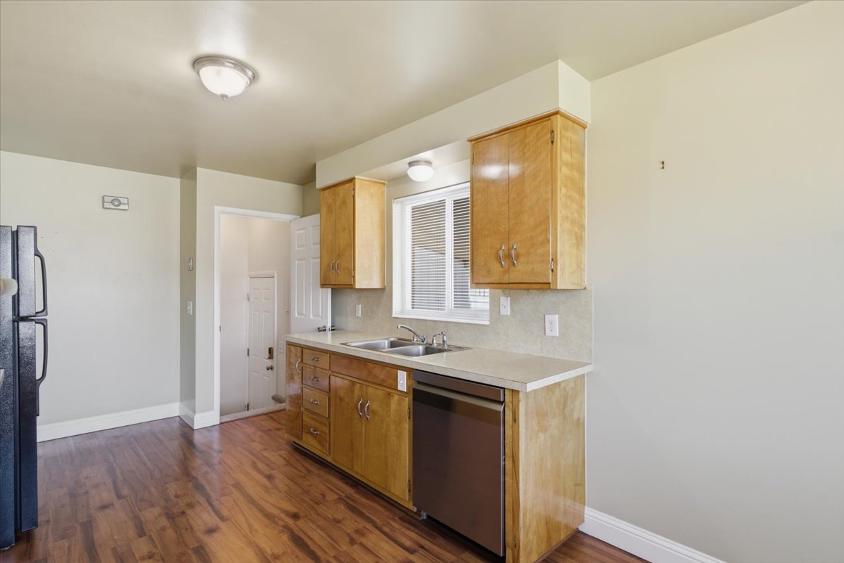 Kitchen featuring wood-finish flooring, light-toned cabinetry, a stainless steel dishwasher, a double basin sink, and a window with blinds