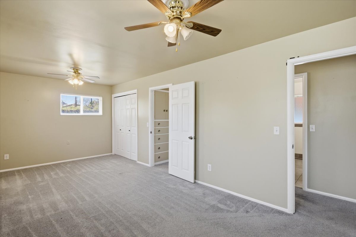 Spacious room featuring neutral wall tones, grey carpeting, two ceiling fans, and bi-fold closet doors