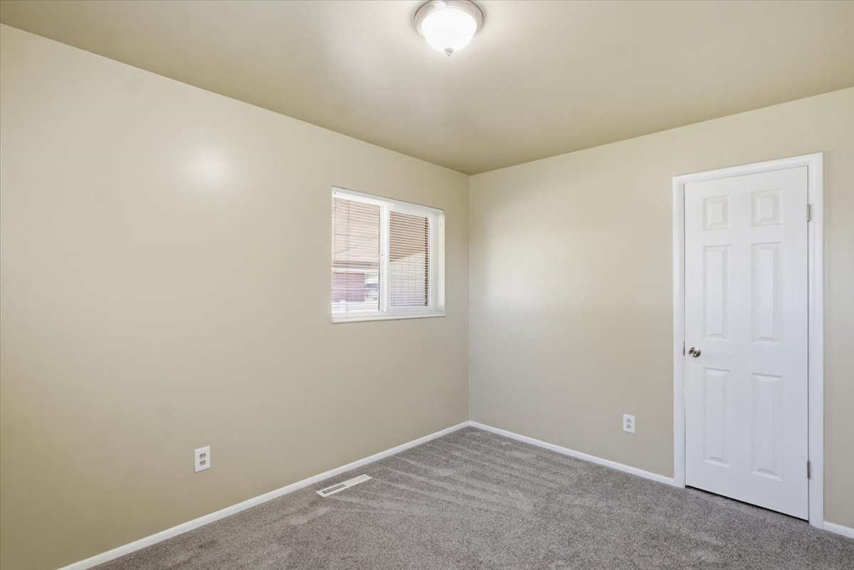 Interior room featuring neutral wall paint, gray patterned carpeting, white baseboards, and a white six-panel door with a round silver-toned knob