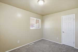 Interior room featuring neutral wall paint, gray patterned carpeting, white baseboards, and a white six-panel door with a round silver-toned knob