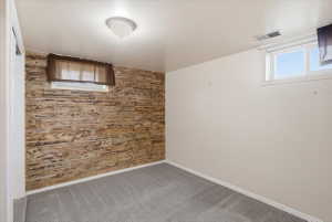 Accent wall featuring natural wood-look paneling, gray carpet flooring, white baseboards, and a flush-mount ceiling light