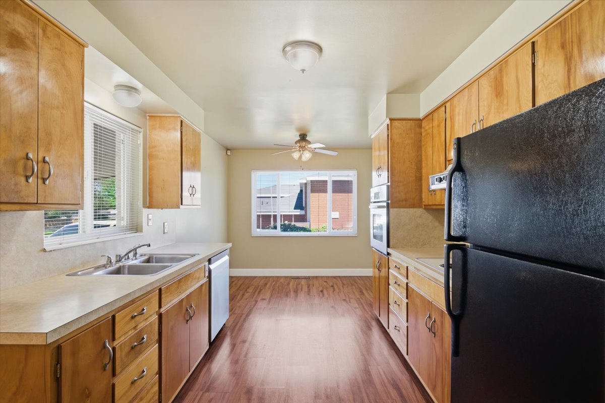 Galley kitchen featuring wood cabinetry, laminate countertops, a double basin stainless steel sink, and wood-finish flooring