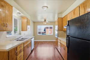Galley kitchen featuring wood cabinetry, laminate countertops, a double basin stainless steel sink, and wood-finish flooring