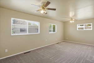 Spacious room featuring neutral-toned walls, ceiling fans with integrated lighting, multiple windows with blinds, and patterned carpet flooring