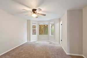 Carpeted room featuring a bay window, ceiling fan with integrated lighting, and neutral wall paint