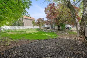 Expansive backyard featuring a large green space, a white privacy fence, mature trees, and a rock retaining wall
