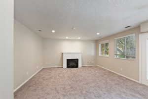 Spacious room featuring a fireplace with a white mantel, recessed lighting, two windows with blinds, and a door with a glass panel