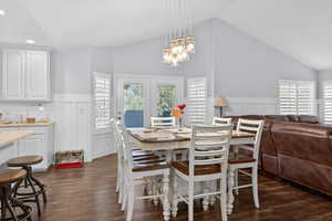 Vaulted ceilings define this dining area, featuring wood-finish flooring, a contemporary multi-light chandelier, and wainscoting detail