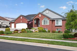 Brick exterior with an arched entry, multiple garage bays, and a well-manicured lawn with mature landscaping
