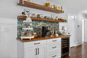 Built-in beverage station featuring white cabinetry, wood-finish countertops, a mosaic tile backsplash, and integrated wine refrigeration