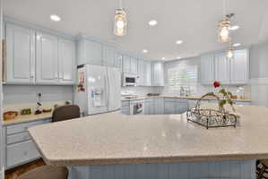 Spacious kitchen featuring light blue cabinetry, built-in appliances, recessed lighting, and a large countertop island