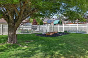 Expansive green lawn with a mature shade tree, white picket fencing, and a landscaped garden bed featuring wood planters