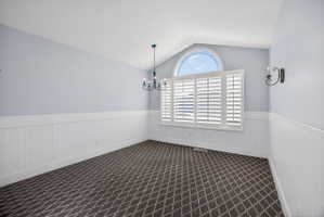 Arched window with plantation shutters, vaulted ceiling, and decorative chandelier