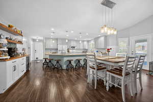 Open-concept kitchen and dining area featuring wood-finish flooring, a spacious kitchen island with seating, light cabinetry, and an integrated beverage cooler