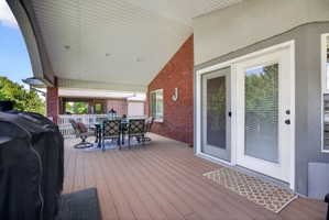 Spacious covered deck featuring composite decking, brick exterior wall, recessed lighting, and white French doors with screen