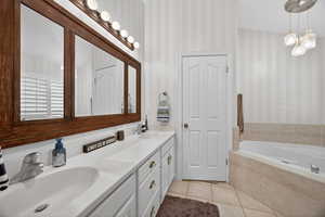 Bathroom featuring a double vanity with white cabinetry, a large framed mirror, and a built-in tub with tile surround