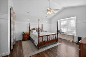 Vaulted ceiling bedroom featuring wood-finish flooring and a window seat with plantation shutters