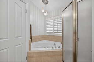 Corner soaking tub with tile surround, plantation shutters, and a frameless glass shower enclosure