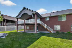 Spacious backyard featuring a manicured lawn, an upper-level deck with white railings, and a covered patio below