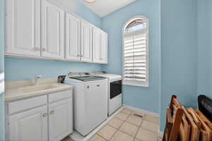 Laundry room with white upper and lower cabinetry, utility sink, and tiled flooring