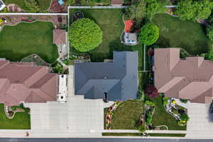 Expansive lot featuring a large dark-shingled roof, extensive concrete paving, varied landscaping with mature trees, and a manicured lawn