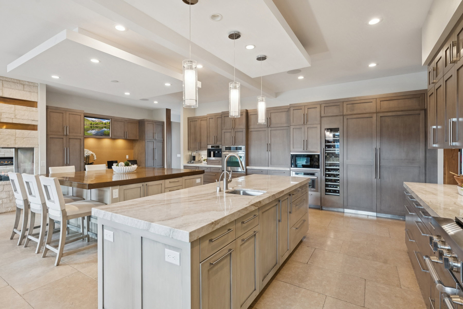 Spacious kitchen featuring two islands with stone countertops, integrated stainless steel appliances, extensive wood-finish cabinetry, and recessed ceiling lighting