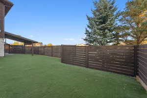 Expansive artificial turf backyard featuring a dark wood horizontal slat fence and a covered side patio