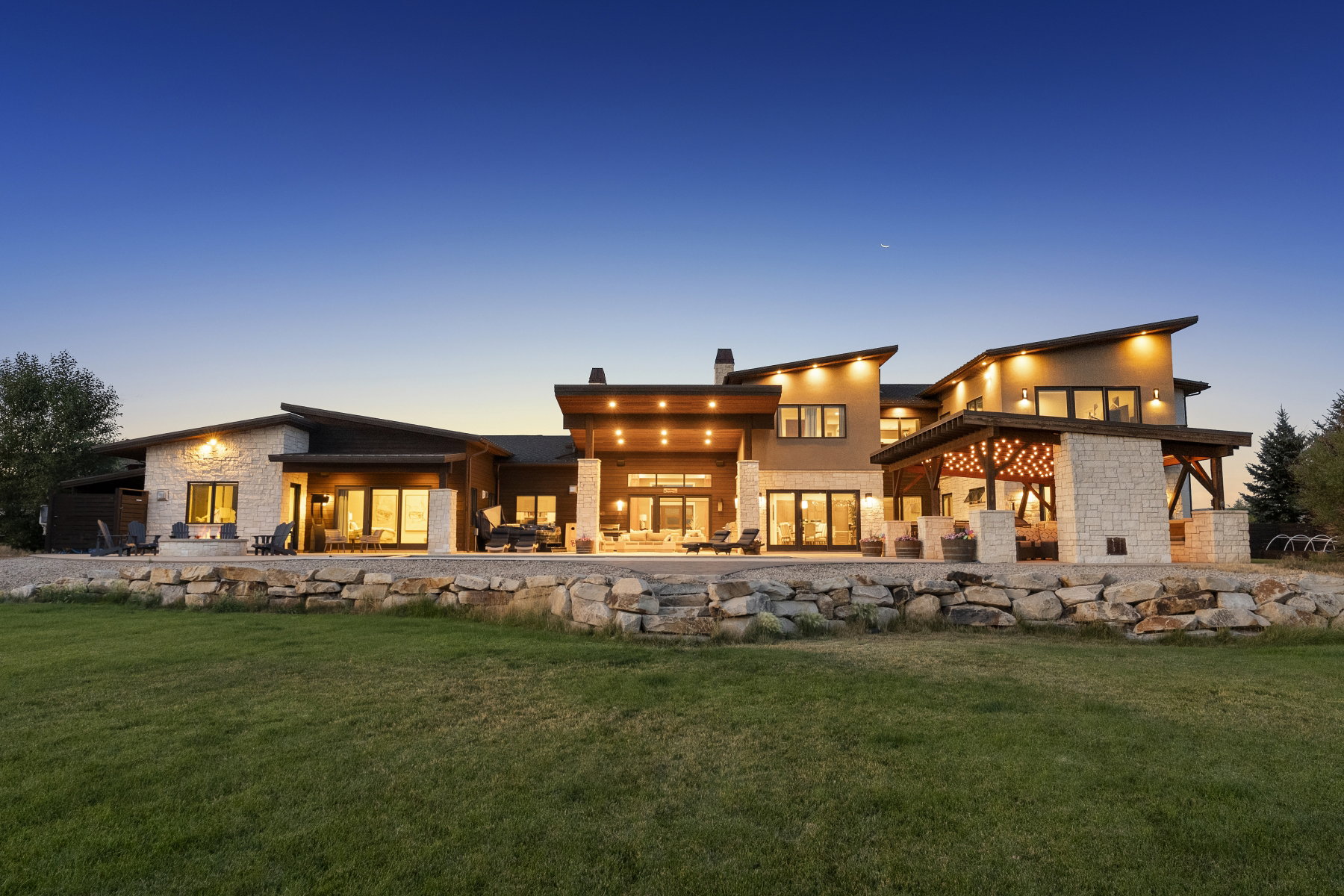 Modern exterior design featuring natural stone accents, extensive glass doors, multiple patios, sloped rooflines, and a covered outdoor living area