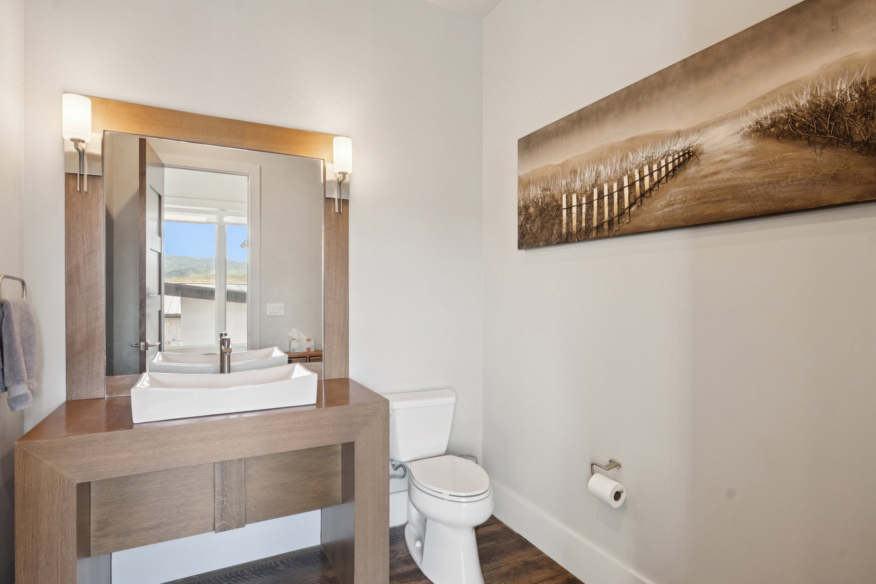 Contemporary bathroom featuring a rectangular vessel sink, a wood-finish vanity, a mirrored vanity with sconce lighting, a white toilet, and wood-finish flooring
