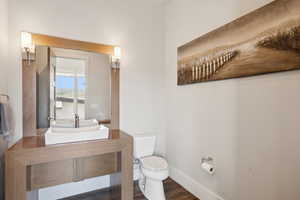Contemporary bathroom featuring a rectangular vessel sink, a wood-finish vanity, a mirrored vanity with sconce lighting, a white toilet, and wood-finish flooring