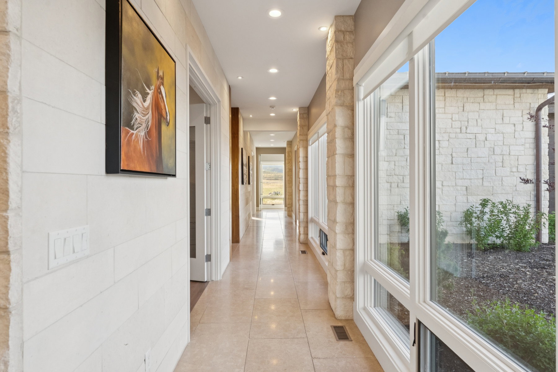 Hallway featuring light-toned stone tile flooring, recessed lighting, and white horizontal wall paneling