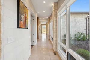 Hallway featuring light-toned stone tile flooring, recessed lighting, and white horizontal wall paneling