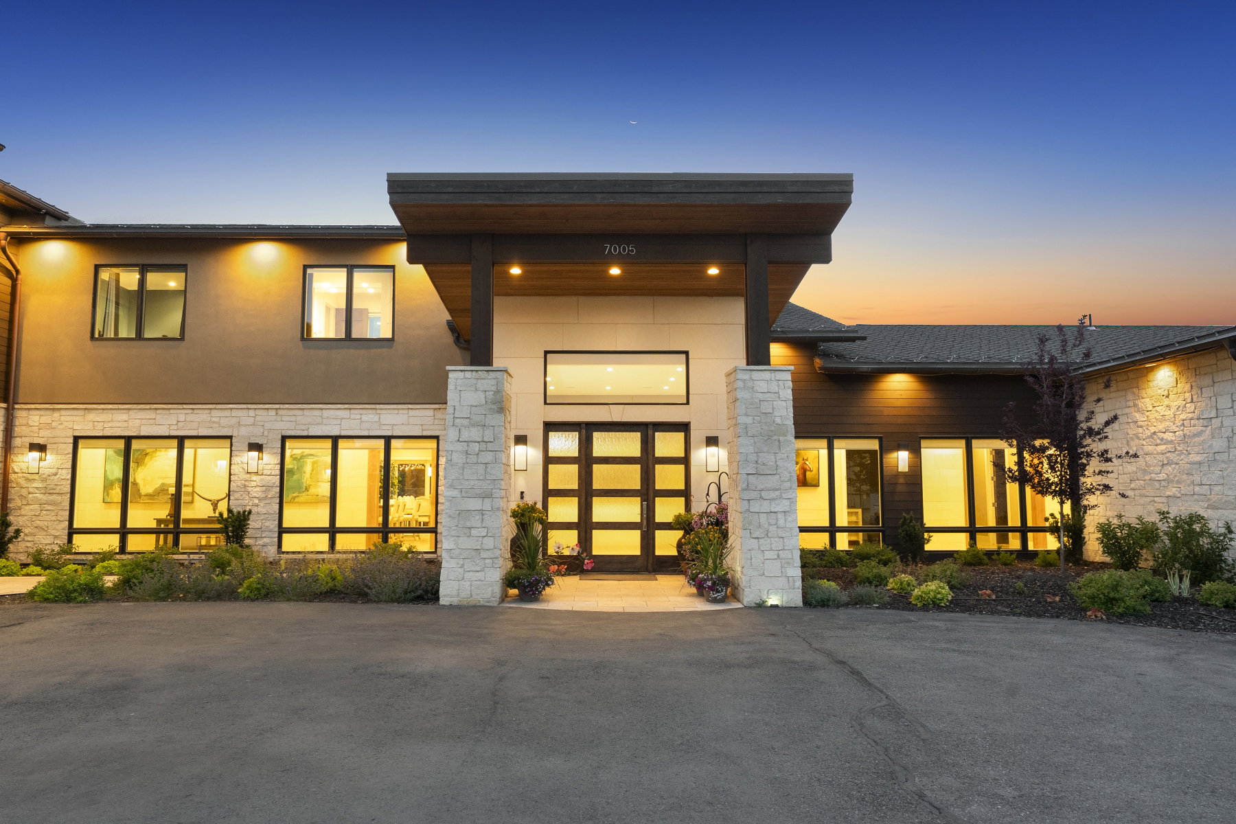 Contemporary exterior featuring a prominent covered entry with dark wood accents, stone columns, and double glass-paneled doors