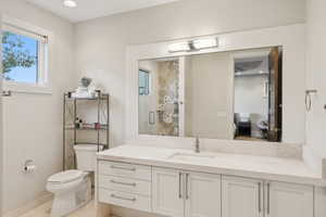 Bathroom featuring a double vanity with white cabinetry and integrated sink, a large framed mirror with overhead lighting, a white toilet, and tile flooring