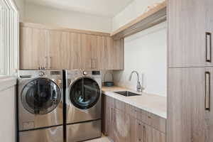 Dedicated laundry space featuring a window, built-in wood-finish cabinetry, stainless steel sink with gooseneck faucet, light-toned countertop, and integrated hanging rod