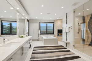 Spacious bathroom featuring a dual vanity with undermount sinks and extensive countertop space, an integrated fireplace with stone surround, a soaking tub, and a glass-enclosed shower with a decorative tile wall