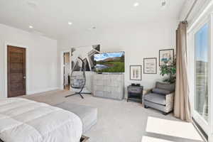 Spacious room featuring light-colored carpeting, recessed lighting, and a dark wood-finish door