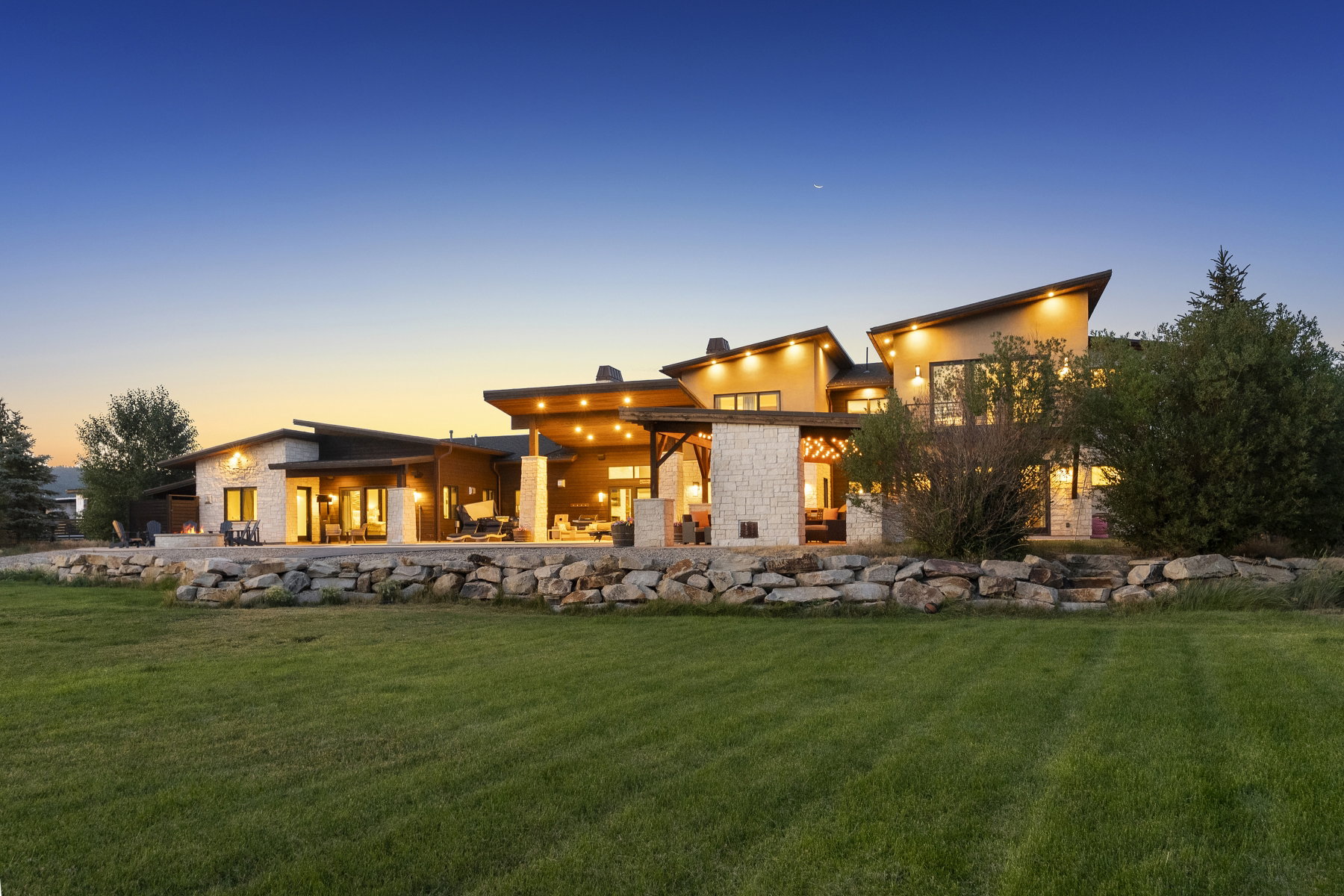 Expansive lawn area fronting a contemporary residence featuring multiple outdoor patio spaces, stone accents, and varied rooflines