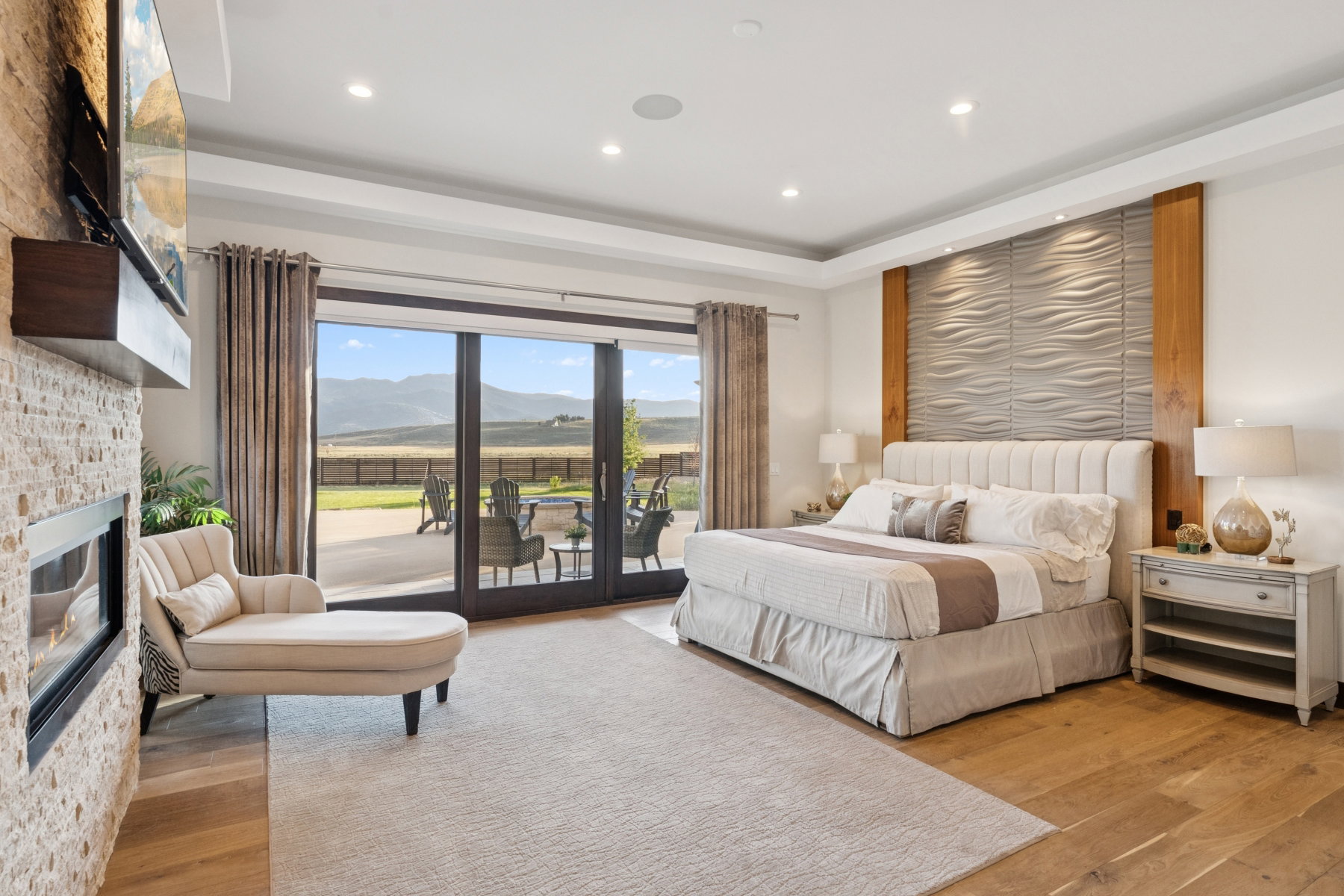 Spacious room featuring wood-finish flooring, a contemporary fireplace with a stone surround, and an accent wall with a textured panel design