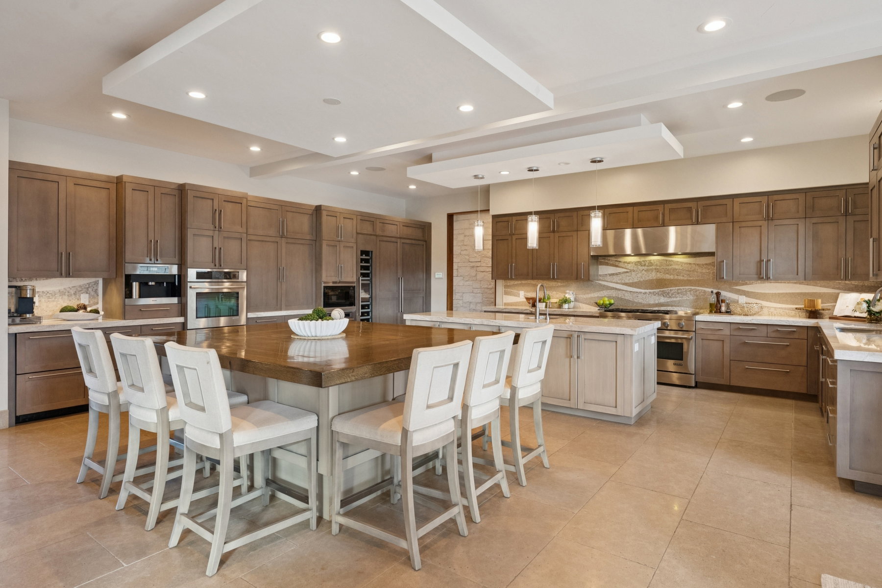 Expansive kitchen featuring a large central island with seating, extensive cabinetry, stainless steel appliances, and tray ceilings with recessed lighting