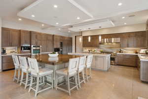 Expansive kitchen featuring a large central island with seating, extensive cabinetry, stainless steel appliances, and tray ceilings with recessed lighting