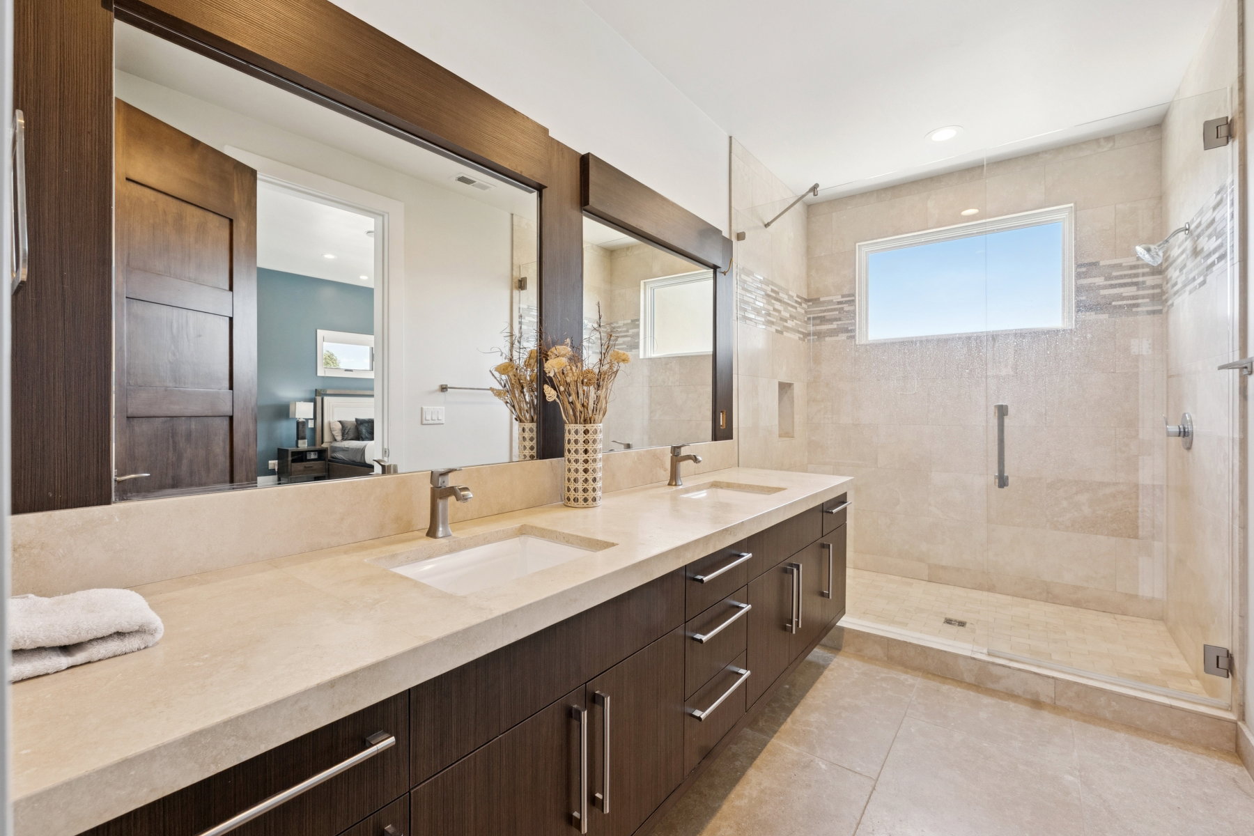 Contemporary bathroom featuring a spacious dual-sink vanity with a light-toned countertop, dark wood-finish cabinetry, and brushed nickel hardware