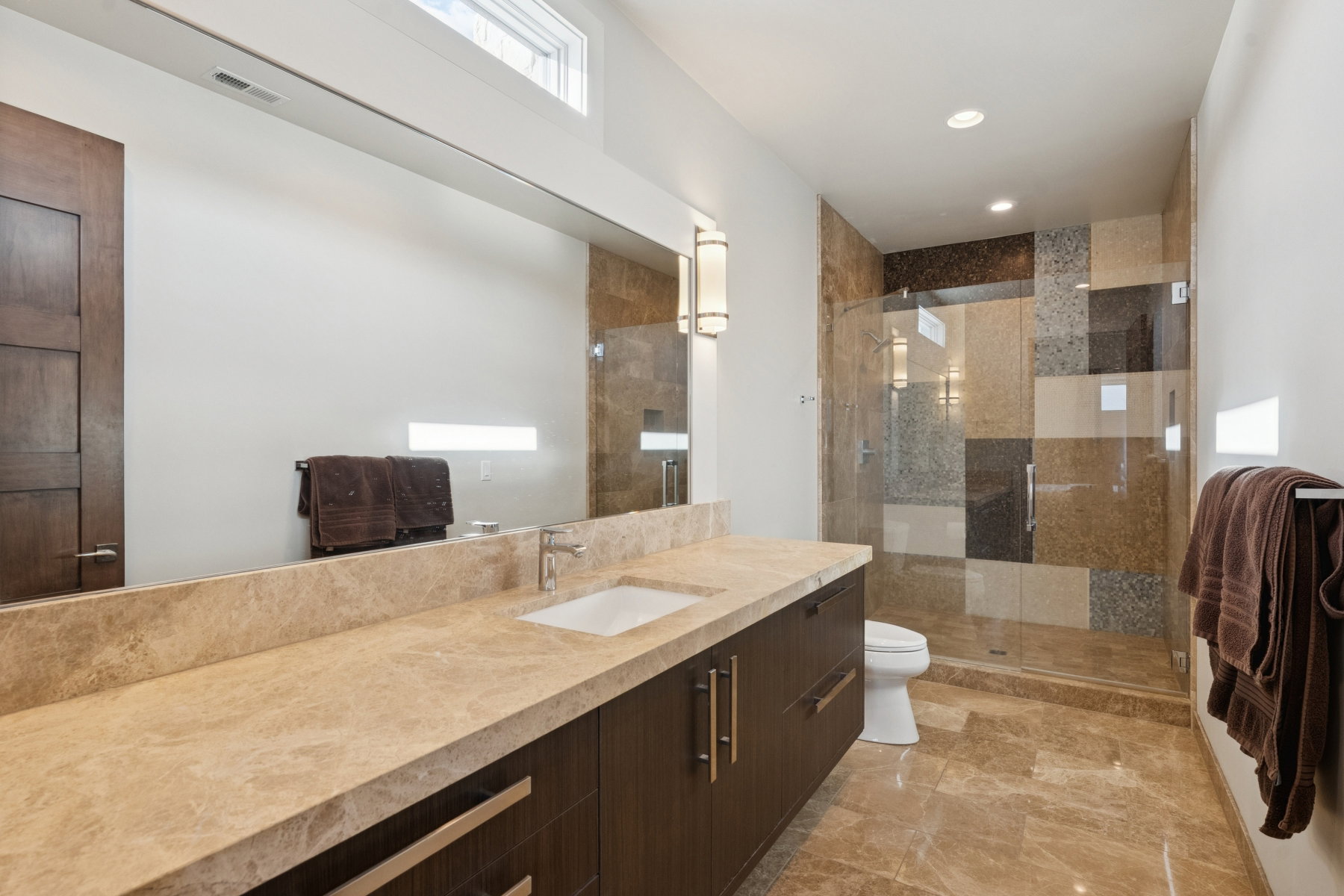 Bathroom featuring a spacious walk-in shower with glass enclosure, a wide vanity with an integrated sink, and stone-finish flooring
