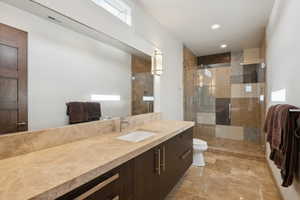 Bathroom featuring a spacious walk-in shower with glass enclosure, a wide vanity with an integrated sink, and stone-finish flooring