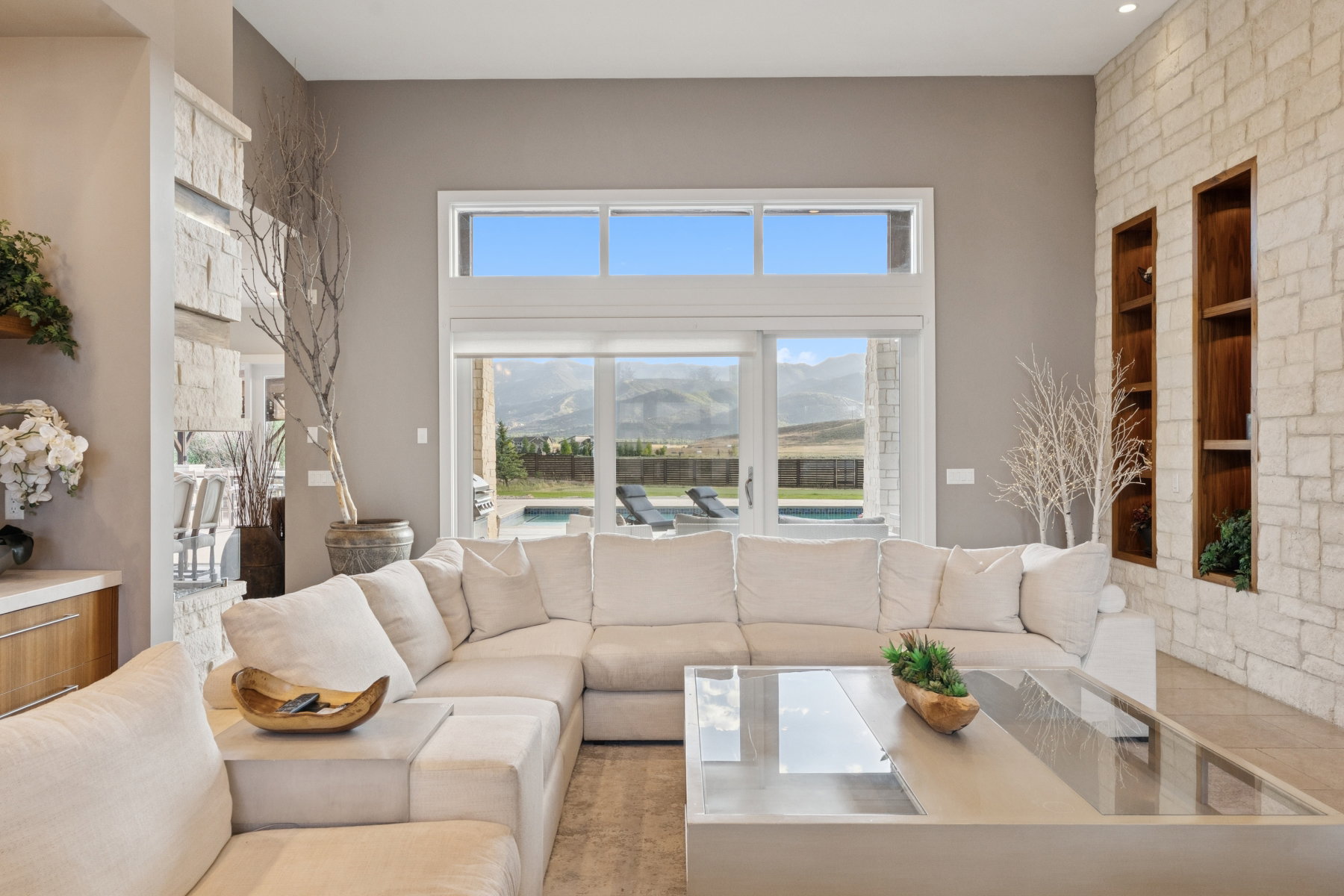 Spacious living area featuring high ceilings, stone accent walls with integrated shelving, and large windows with transom panels