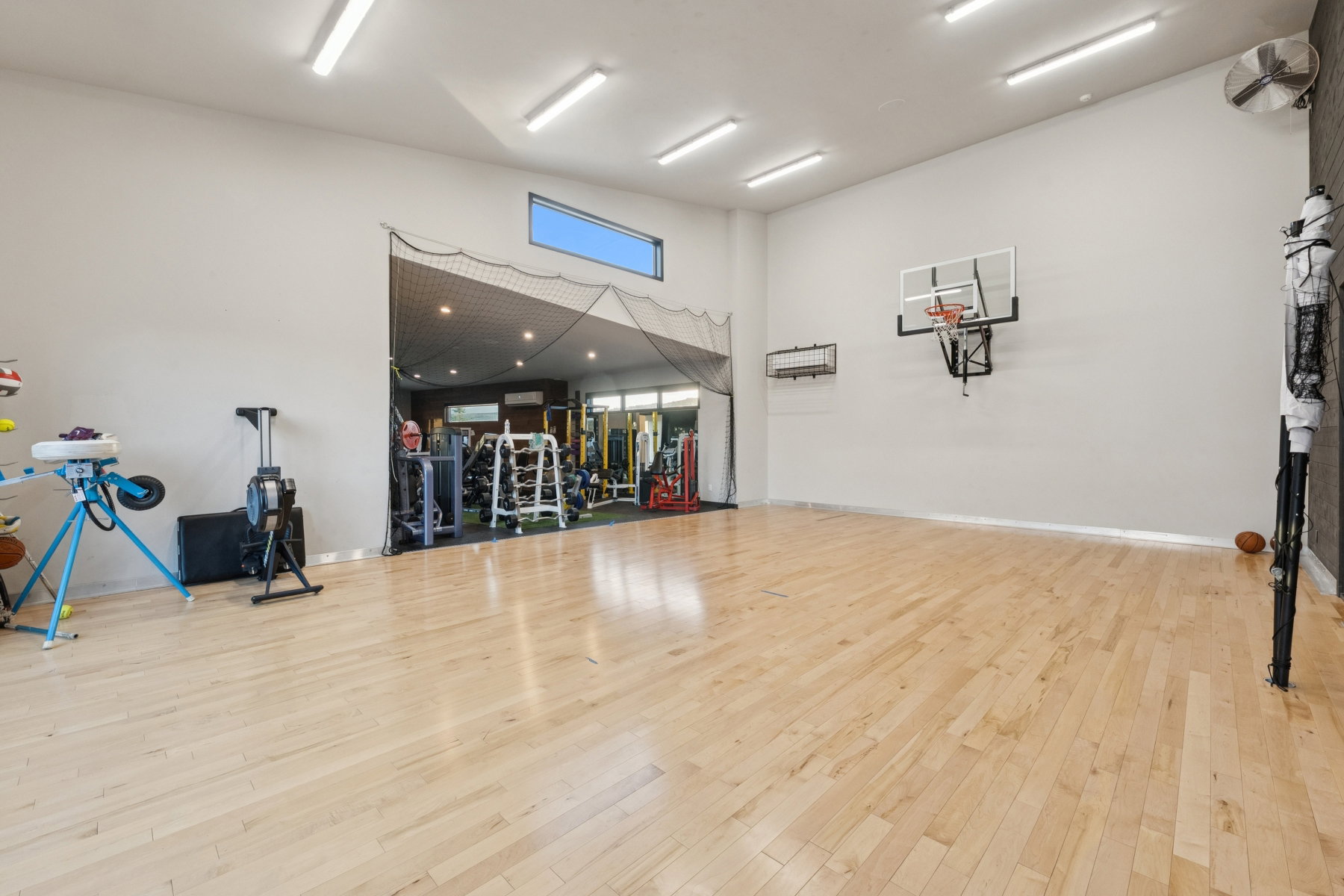 Spacious athletic room featuring wood-finish flooring, a mounted basketball hoop, and high ceilings with linear lighting fixtures