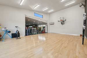Spacious athletic room featuring wood-finish flooring, a mounted basketball hoop, and high ceilings with linear lighting fixtures