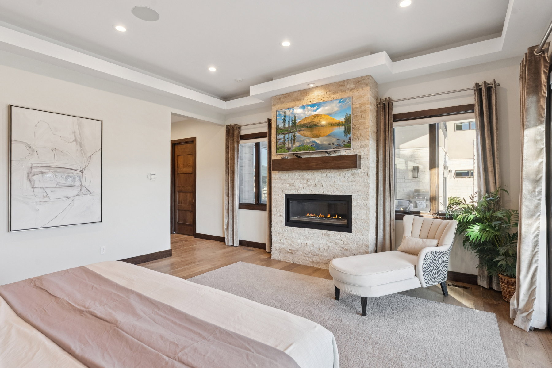 Spacious room featuring a stone-clad fireplace with a built-in television, tray ceiling with recessed lighting, wood-finish flooring, and a solid wood paneled door