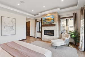 Spacious room featuring a stone-clad fireplace with a built-in television, tray ceiling with recessed lighting, wood-finish flooring, and a solid wood paneled door