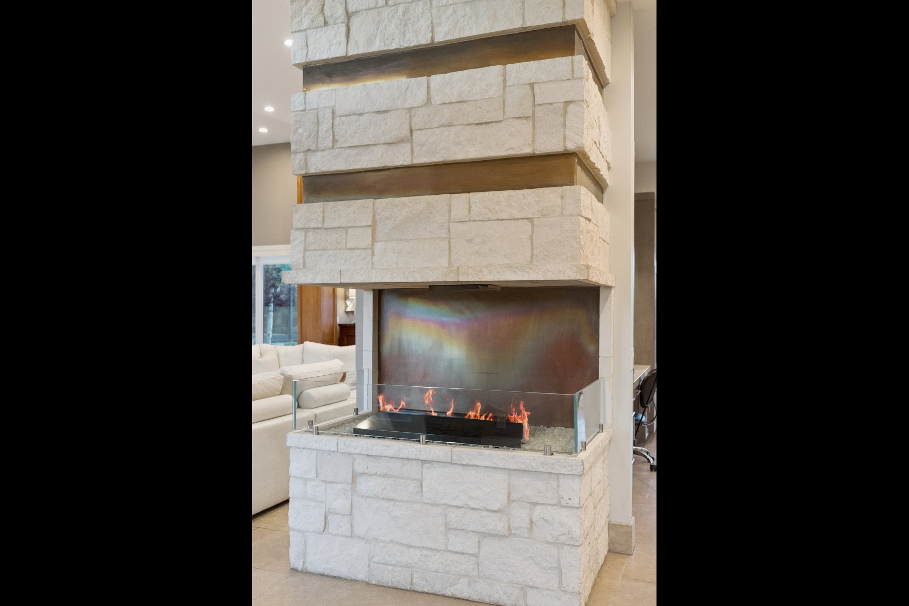 Stone-clad fireplace featuring a multi-sided glass-enclosed firebox and metallic accent bands